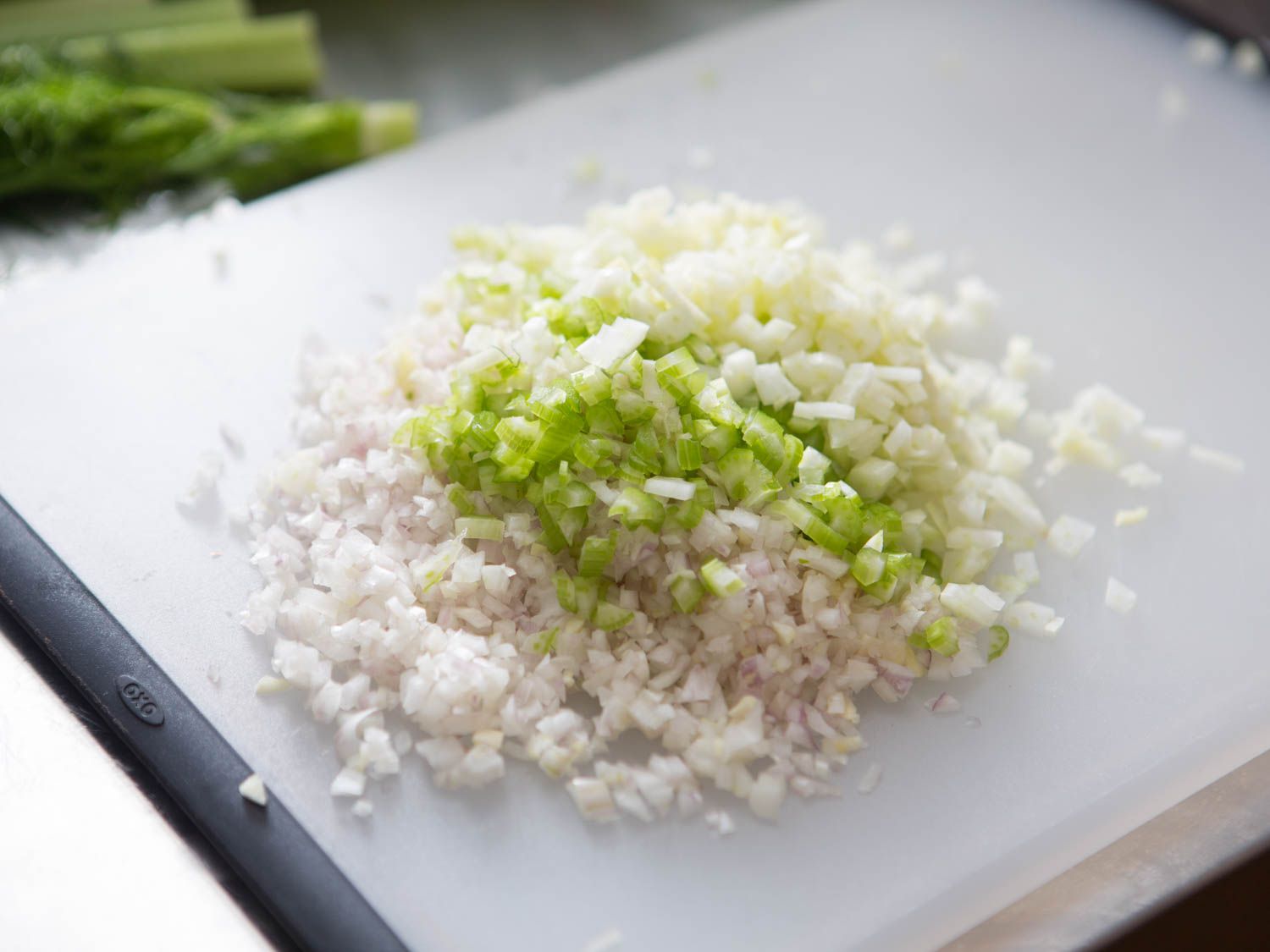 Finely diced shallots, fennel, and celery are piled together on a cutting board.
