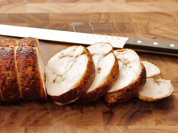 Sliced turkey porchetta (turchetta) on a wooden cutting board with a slicing knife in the background.