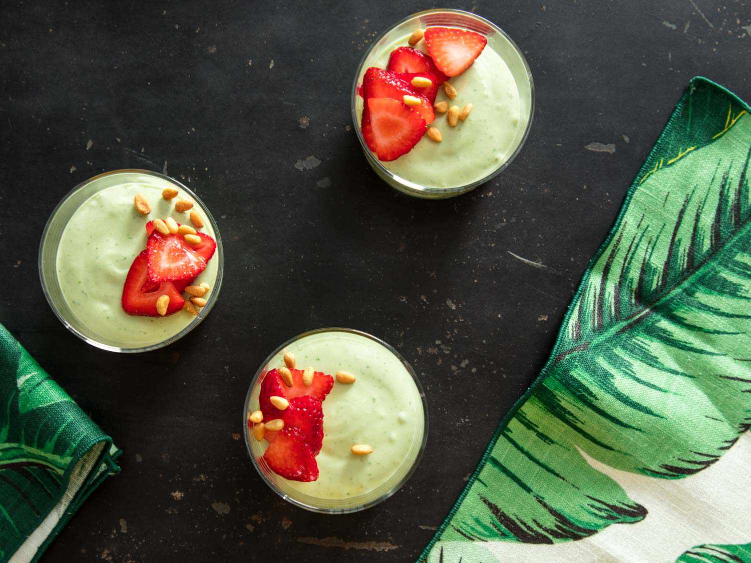Overhead view of glasses filled with fresh basil mousse, garnished with sliced strawberries and toasted pine nuts.