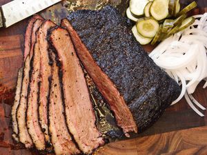Cooked, sliced sous vide brisket on a cutting board with thinly sliced onions and pickles. 