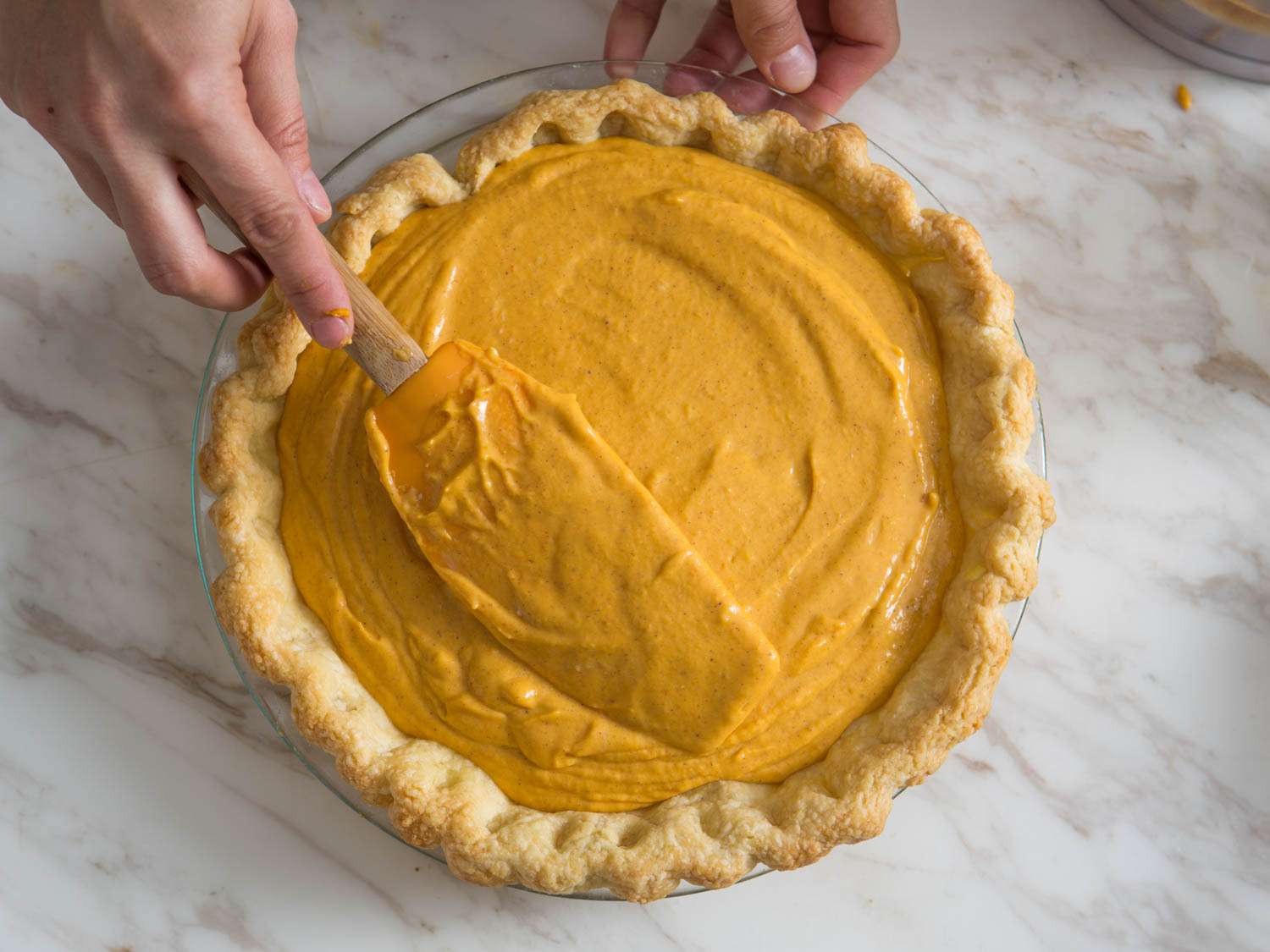 A person spreading pumpkin pie filling into a pie crust with a spatula