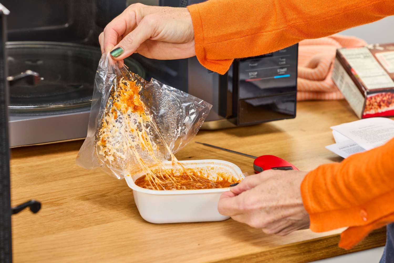 A person removing the film from a meal cooked in the Magic Chef 1.1 Microwave