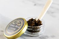 An open jar of Olma kaluga hybrid caviar next to a potato chip topped with crème fraîche and a scoop of caviar