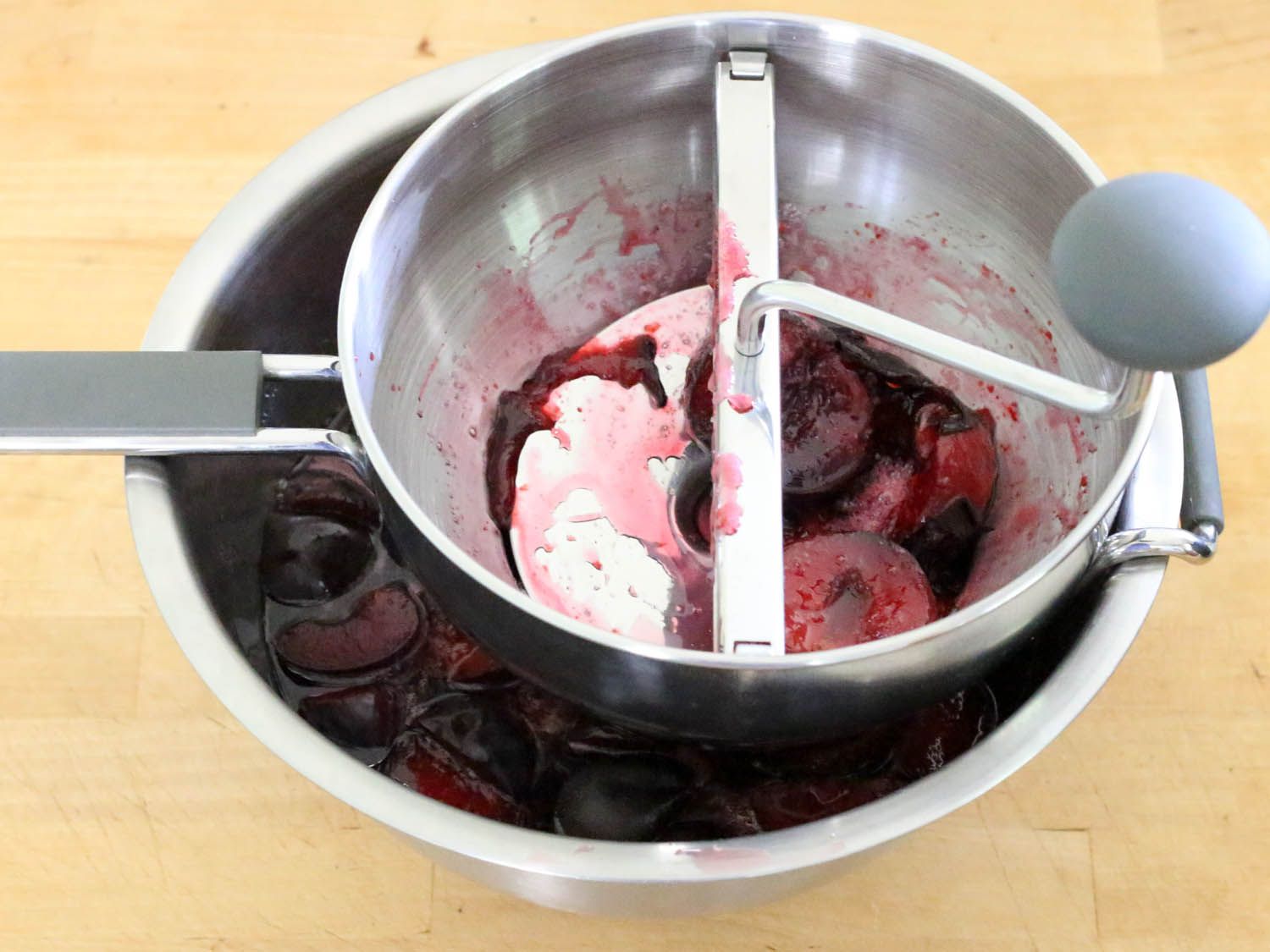 Plums being processed in a hand-cranked food mill. 