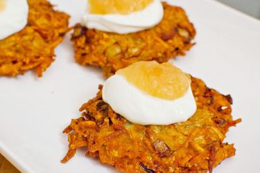 Latkes on a platter topped with sour cream and applesauce.