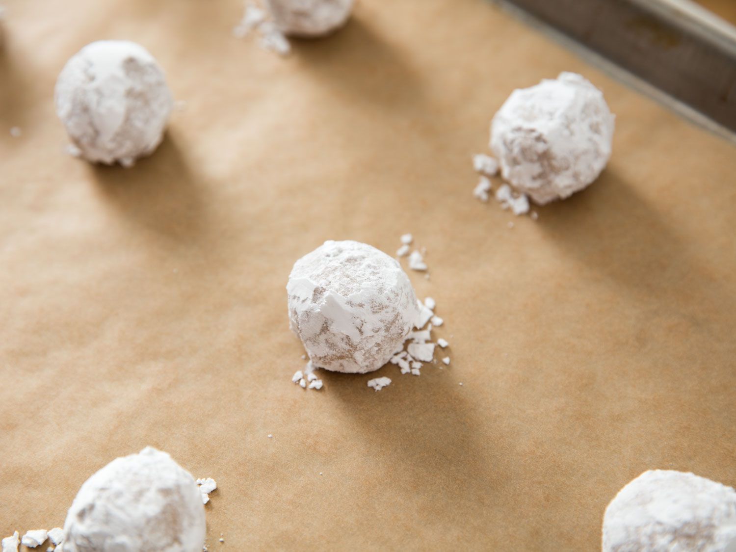 Sugar-coated raw cookie dough balls are placed on a parchment-lined baking sheet.