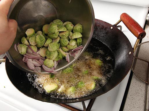Adding Brussels sprouts and shallots to a wok to deep fry.