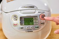 A person presses a button on the Zojirushi Neuro Fuzzy Rice Cooker and Warmer
