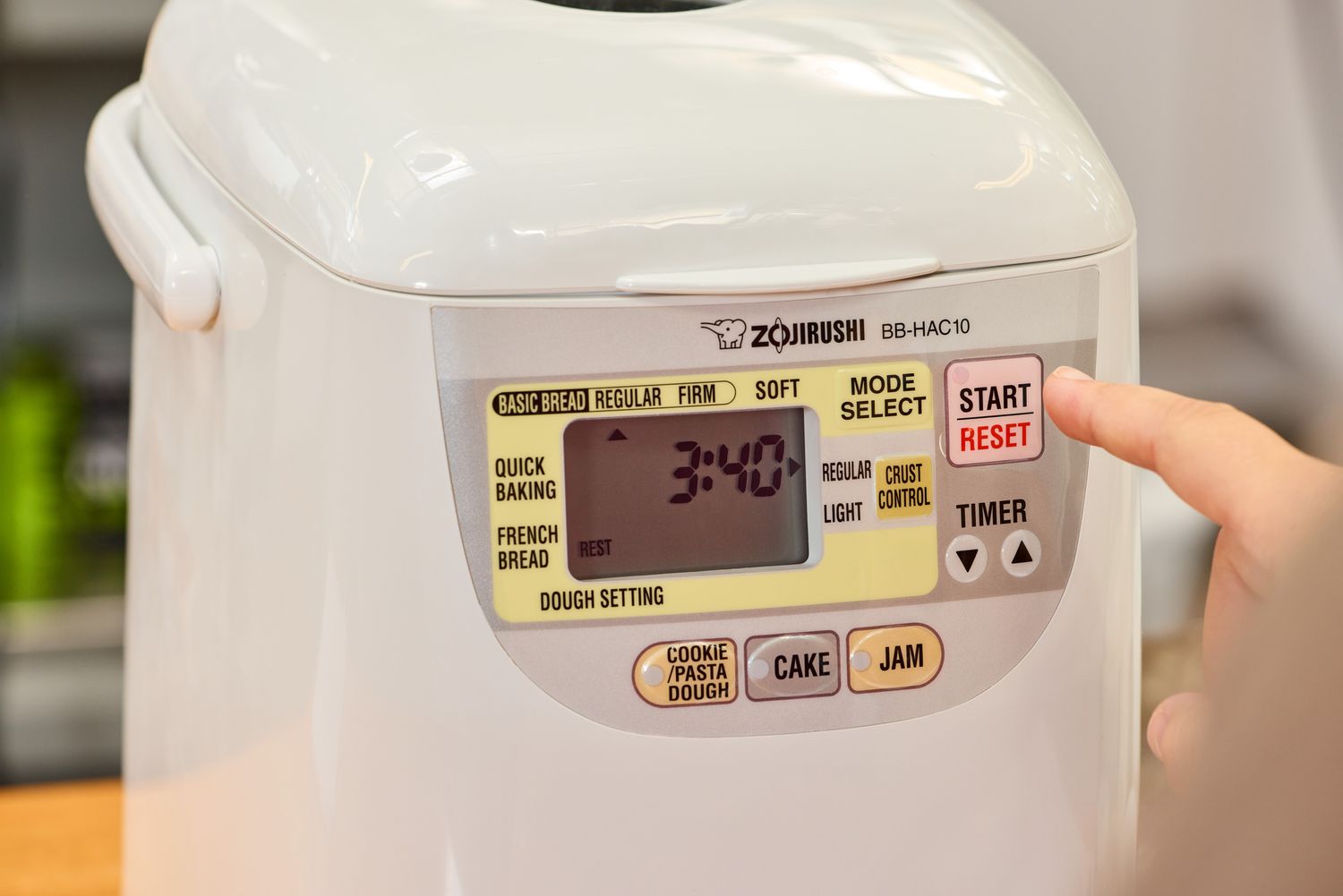 A close-up of a finger pressing a button on the Zojirushi Home Bakery Mini Breadmaker