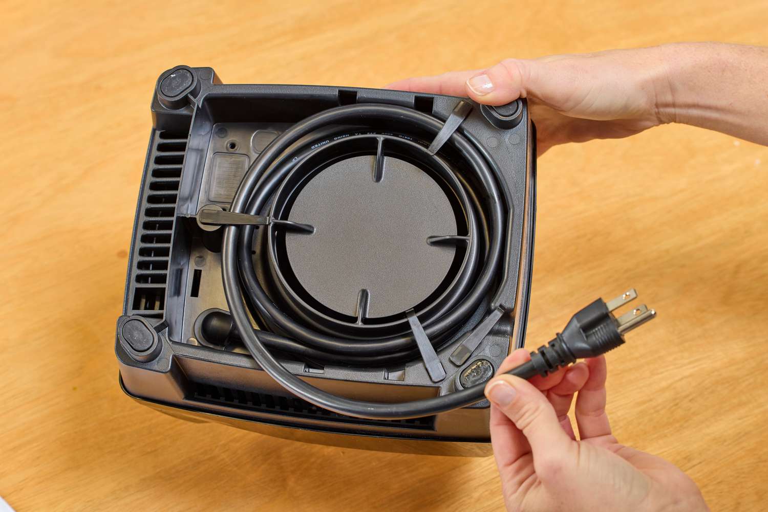 A hand holding the cord on the bottom of the Vitamix E310 Explorian Blender on a wooden background