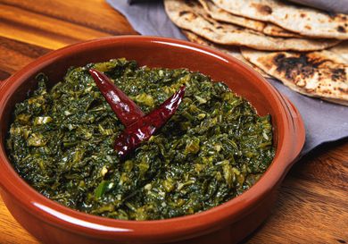 Saag in an earth-toned orange bowl with roti in the background