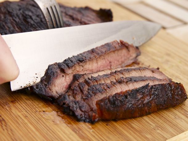 A knife slicing through a flank steak on the cutting board. 