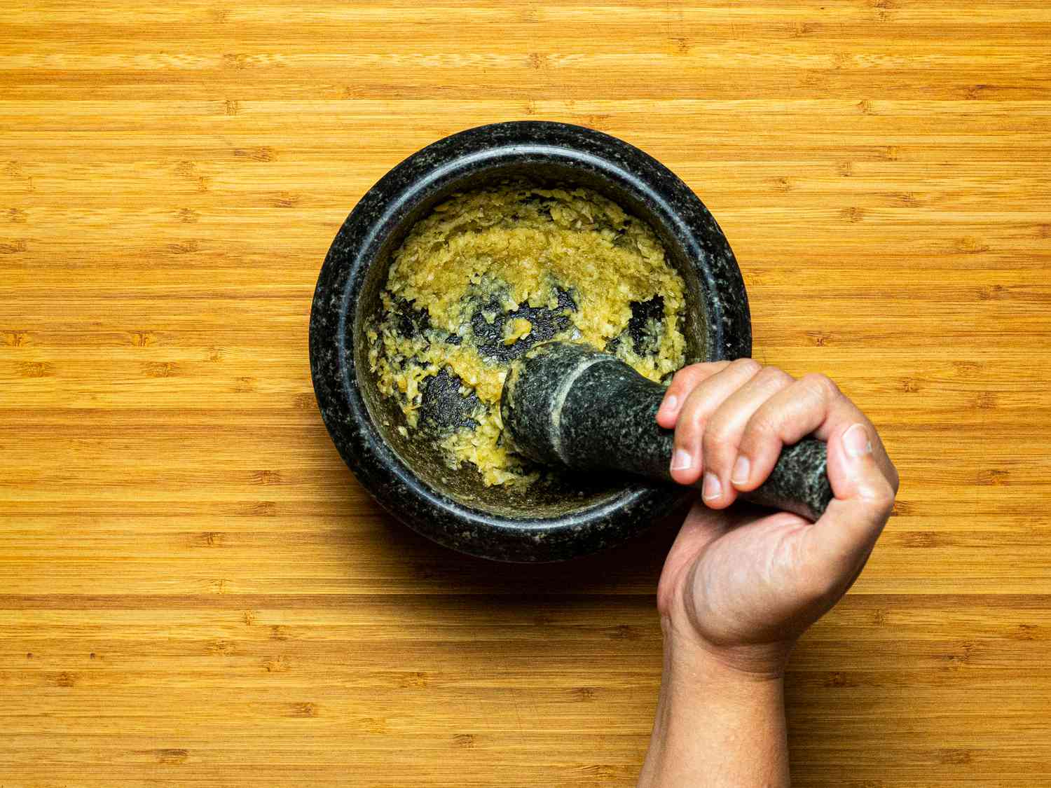 Overhead view of grinding garlic and ginger in mortar 