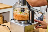 A person chops vegetables in the Magimix 14-Cup Food Processor
