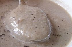 A bowl of mushroom soup with a spoon lifting some of the soup. 
