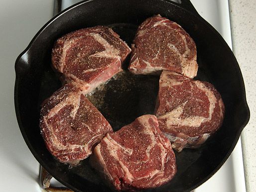 Dry-aged steaks cut in half, frying in a cast iron pan.