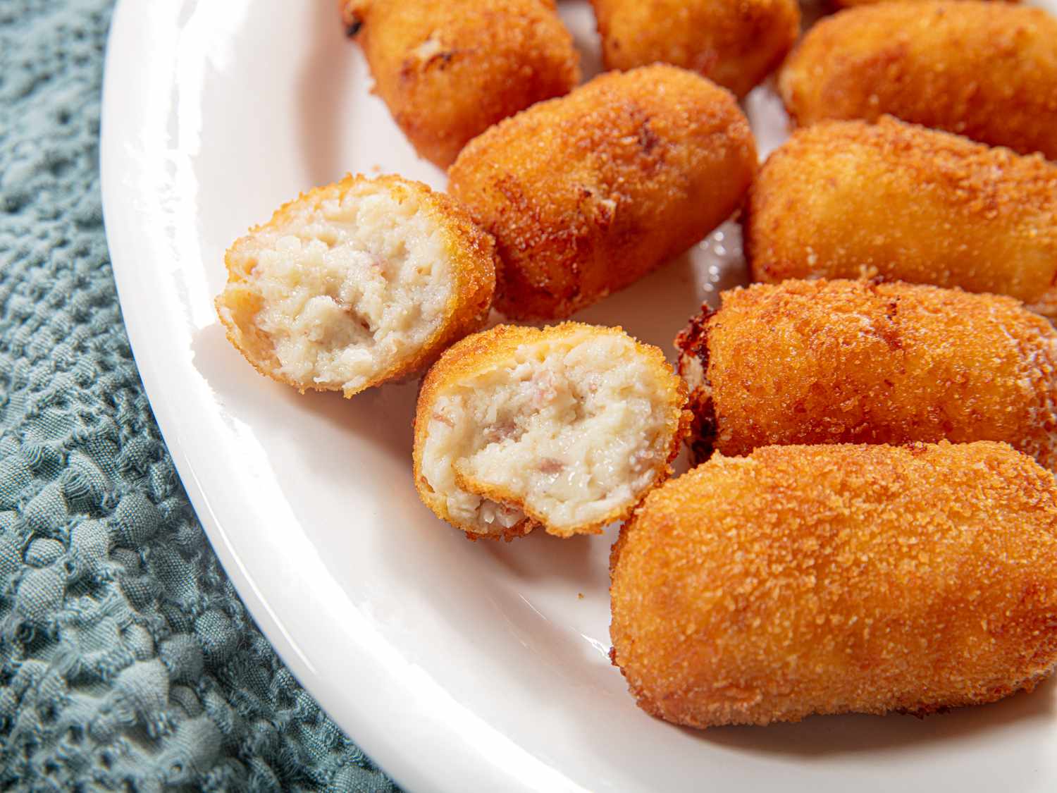 Plate of croquetas with one broken open showing the filling inside