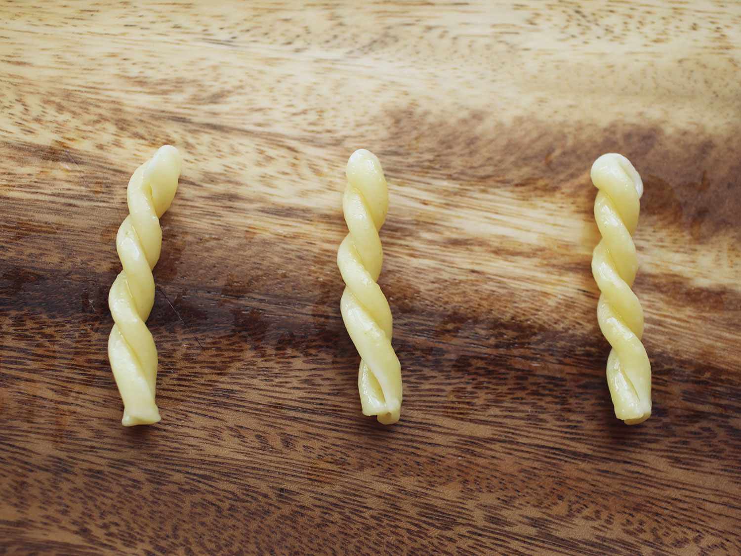 Three pieces of cooked gemelli pasta arranged in parallel on a wooden cutting board.