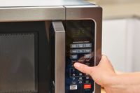 A thumb pressing a button on the Toshiba EM131A5C-BS Microwave Oven