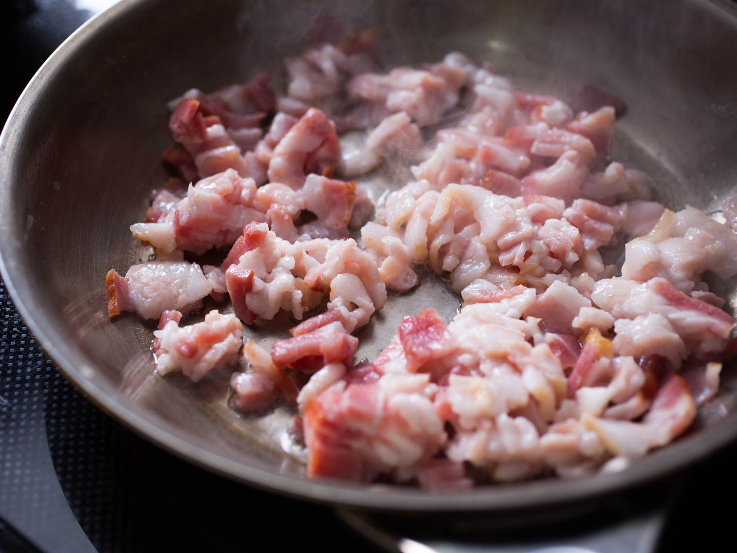 Small cuts of bacon cooking on a stove top.