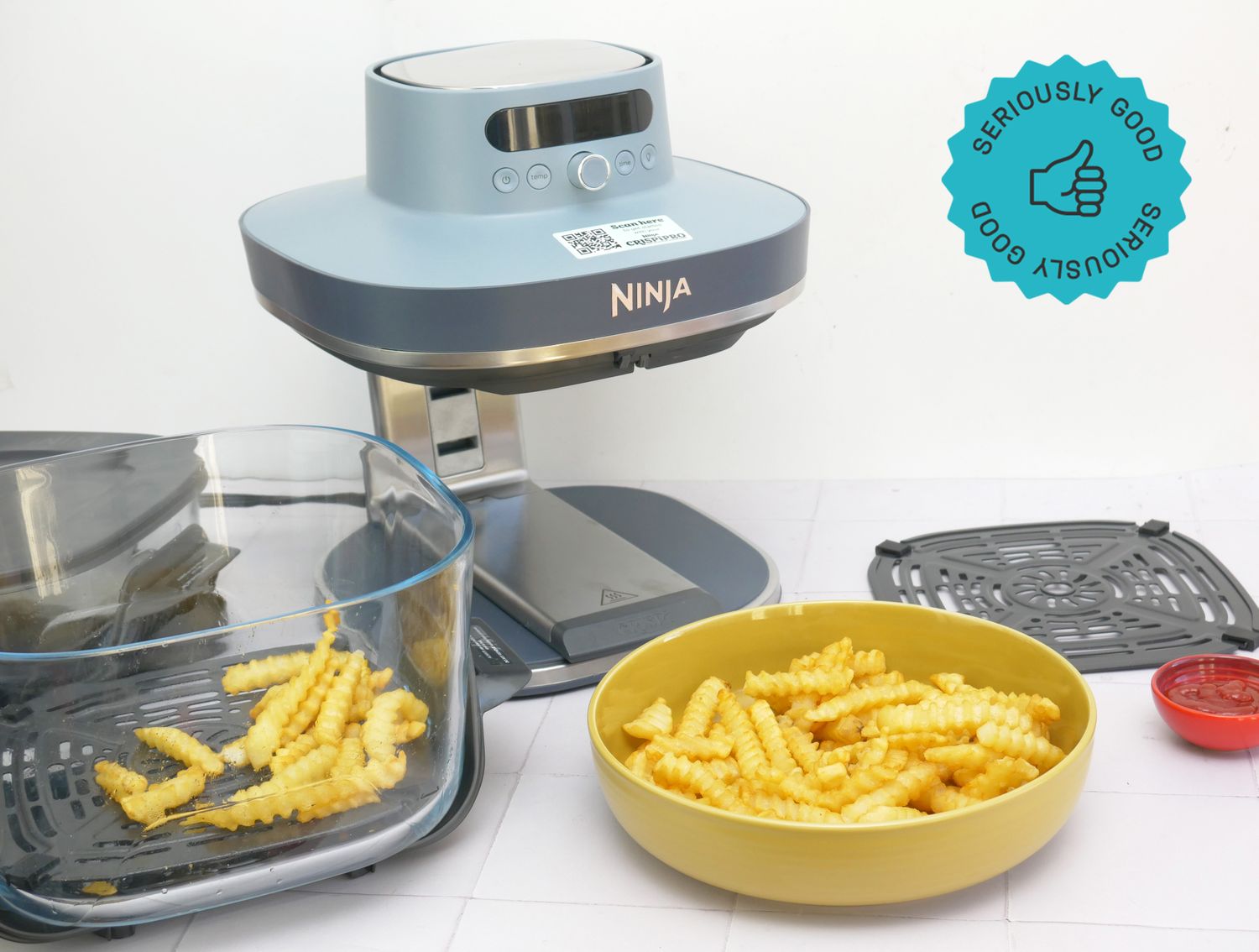 An air fryer with crinklecut fries in a bowl and its glass container nearby showcasing cooking results