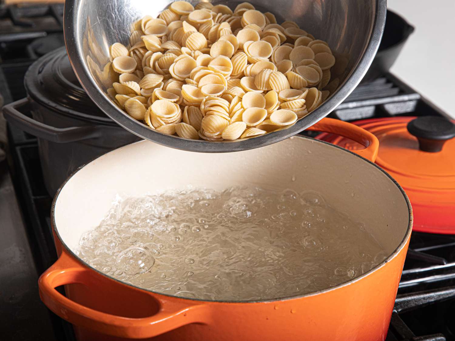 Orecchiette about to go into an orange Dutch oven of boiling water