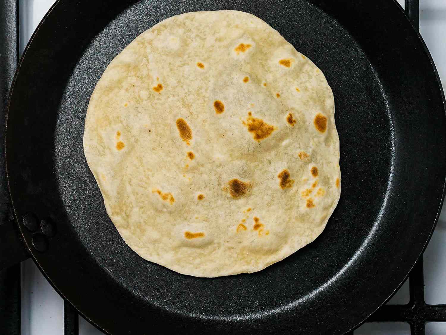 Rewarming a flour tortilla in a cast iron pan to make burritos.