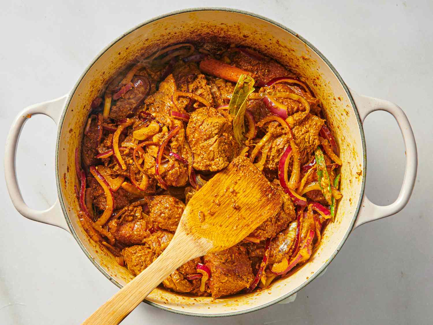 A pot of cooked meat and vegetables with a wooden spoon