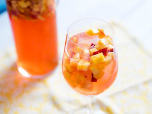 A glass of Sparkling Rosé Sangria With Aperol and Peaches, and a pitcher of the cocktail in the background.