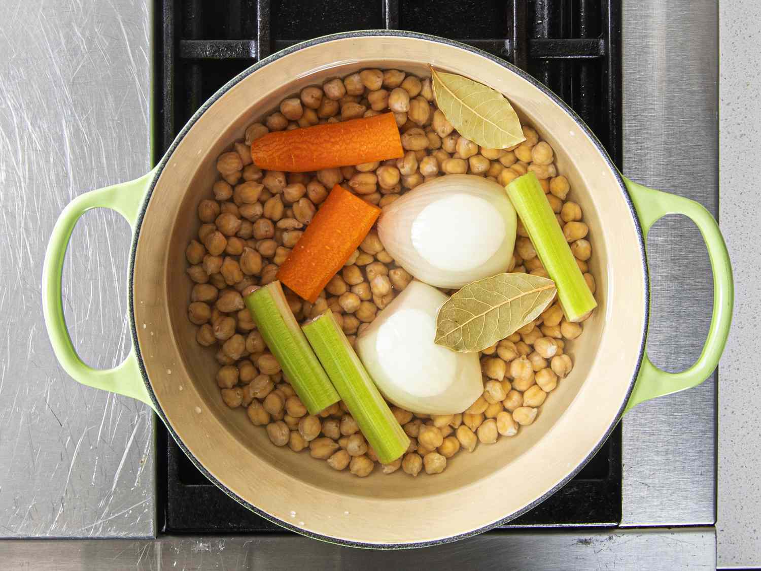Overhead view of chickpeas, onions, celery, and carrots submerged in water in a dutch oven . 
