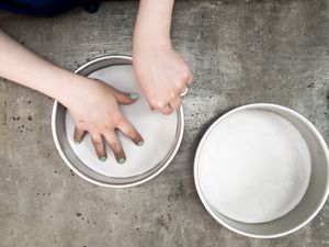 One round cake pan lined with a circle of parchment, hands pressing a circle of parchment into a second cake pan.