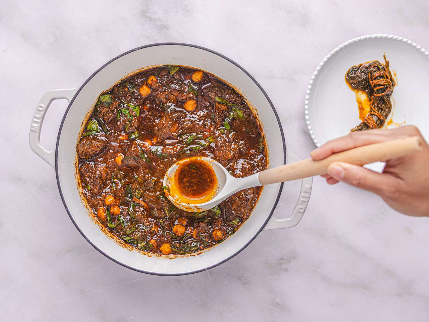 Spoon in dutch oven full of beef stew, with cilantro bundle discarded on the side 