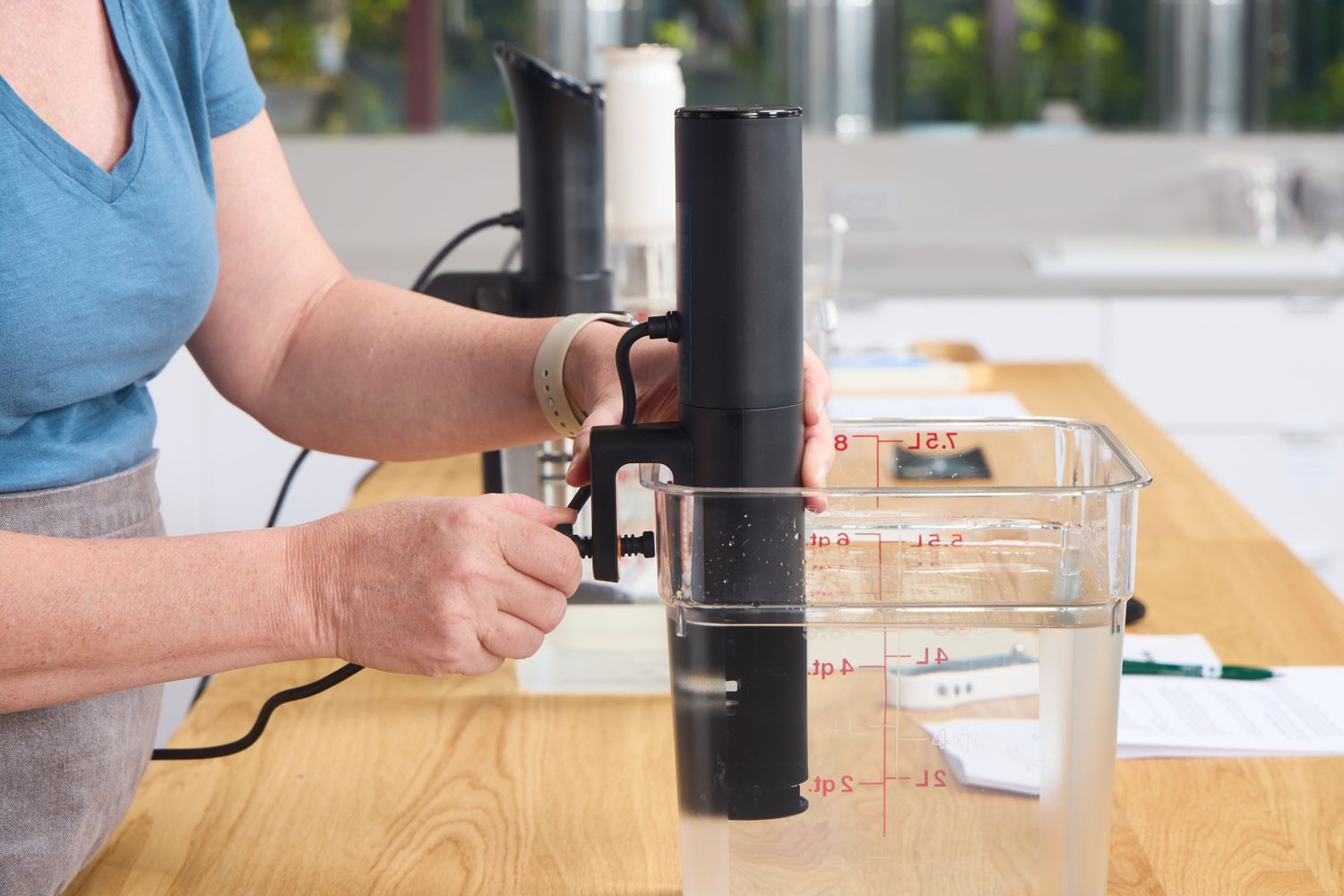 A person attaches a sous vide machine to a plastic Cambro container