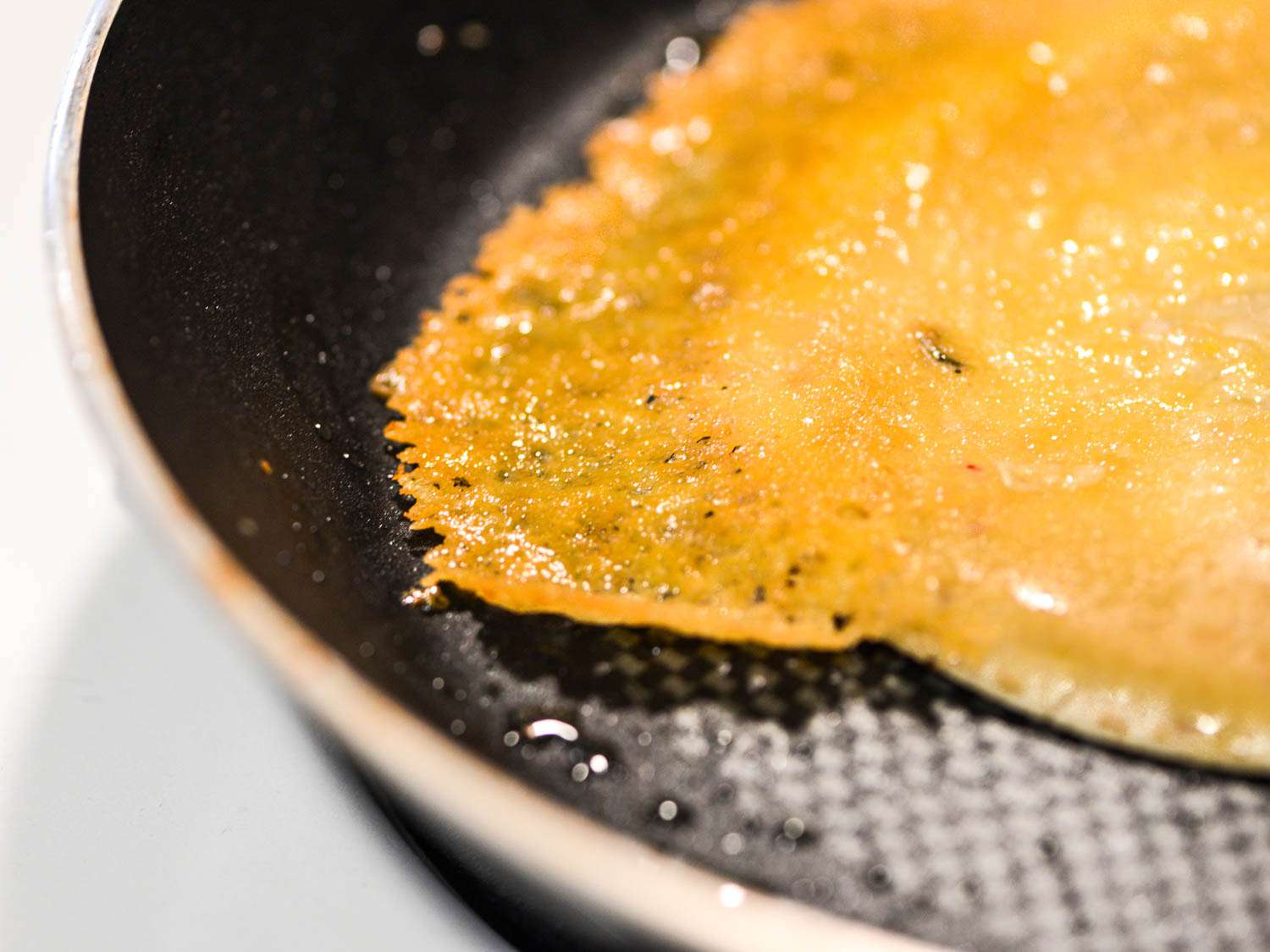 Close-up of lacy crispy pepper jack overhanging a tortilla in a nonstick pan.