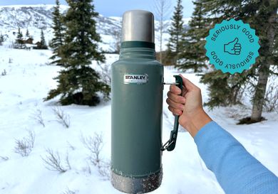 a person holding the stanley thermos in front of the alaskan wilderness