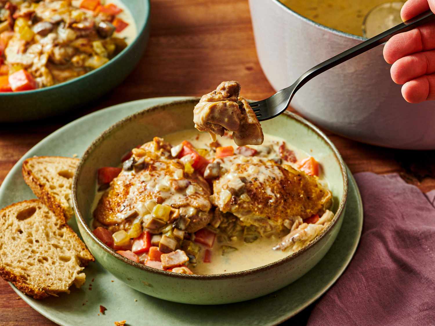 A dish of blanquette de poulet served in a bowl with a fork holding a piece of meat with bread on the side