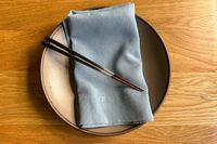 A plate with a folded napkin and a pair of chopsticks resting on it