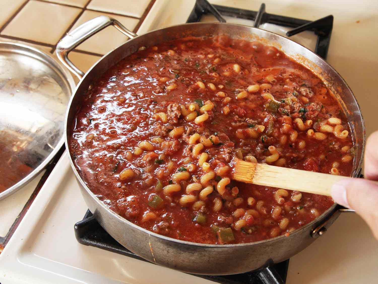 The sauce and pasta being stirred with a wooden spoon.