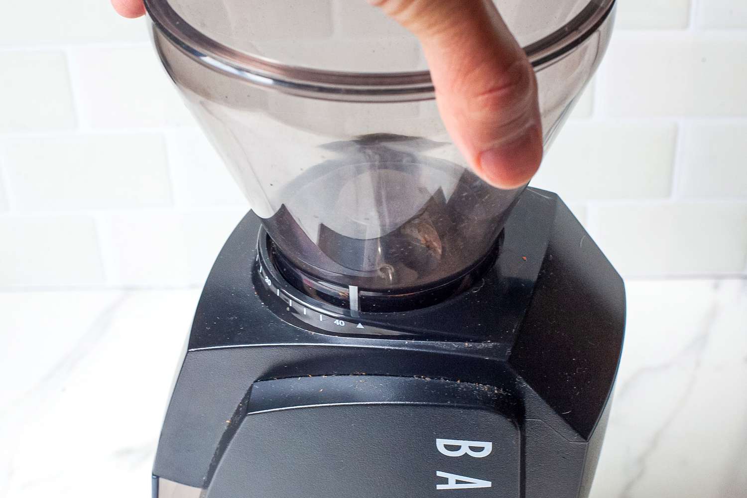 A hand adjusting a coffee grinder's hopper.