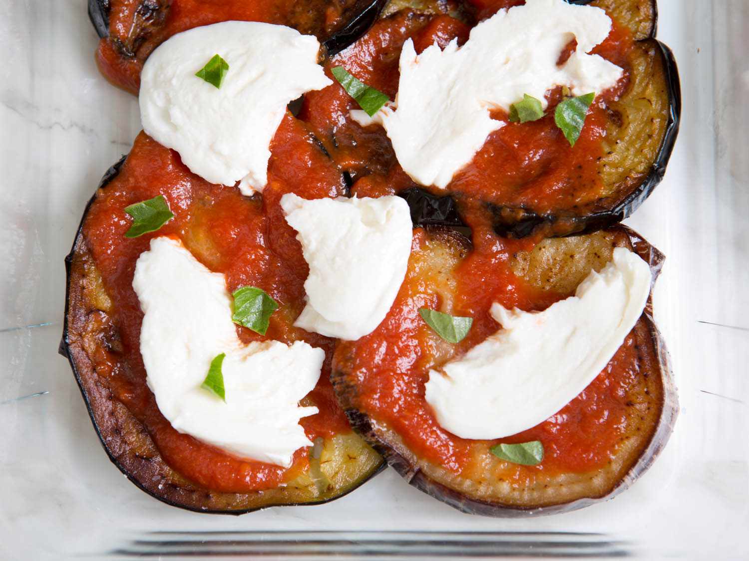Overhead view of eggplant, tomato sauce, and mozzarella layered in a baking dish.