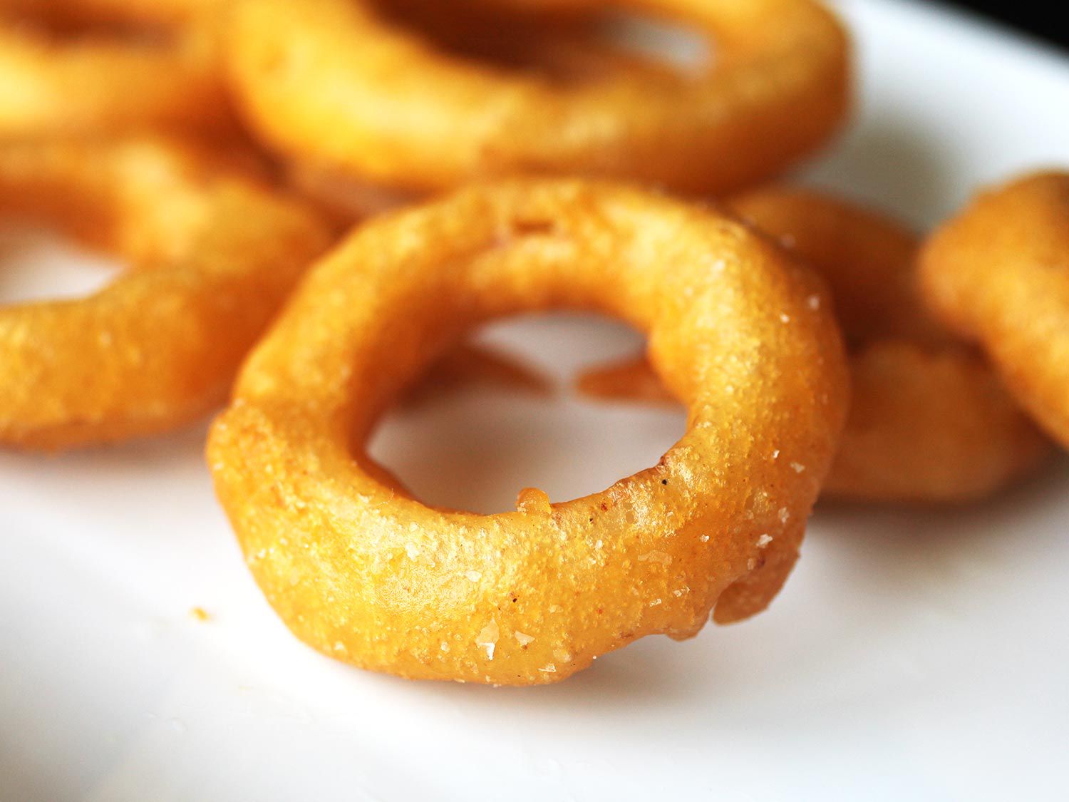 Close-up of a finished onion ring, golden, crispy, and lightly sprinkled with salt.
