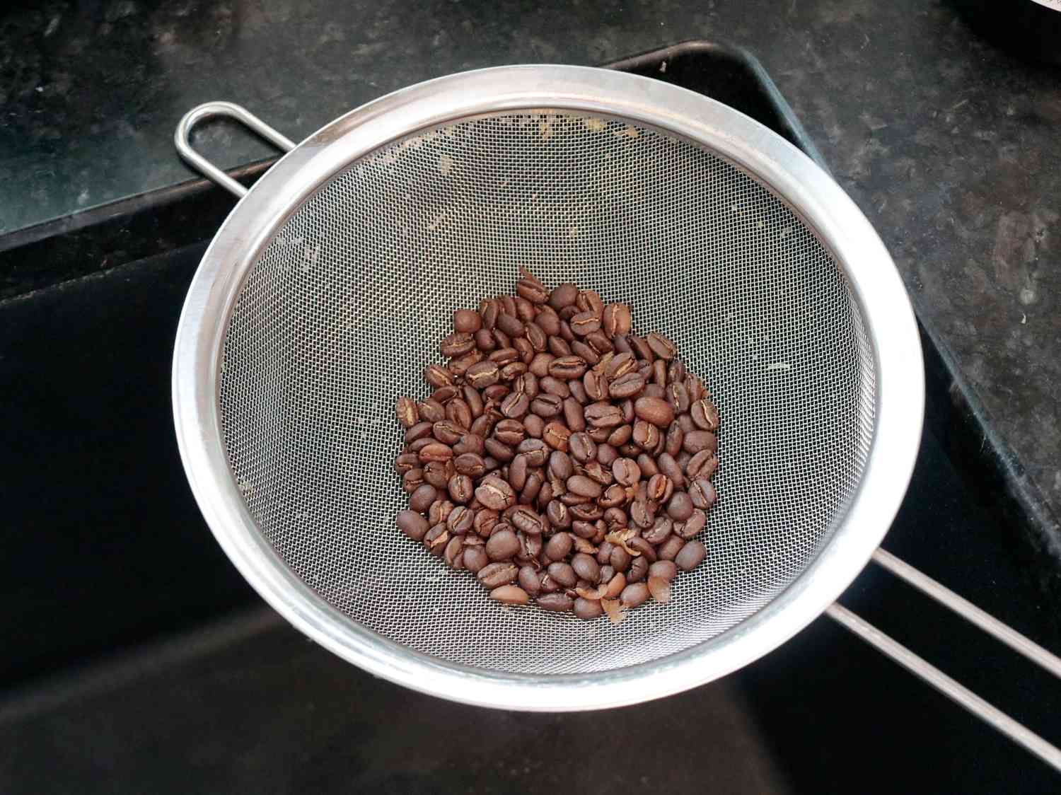 Roasted coffee cooling in a mesh strainer over a sink
