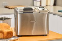The Breville Custom Loaf Bread Maker on the side of a wooden counter next to bread
