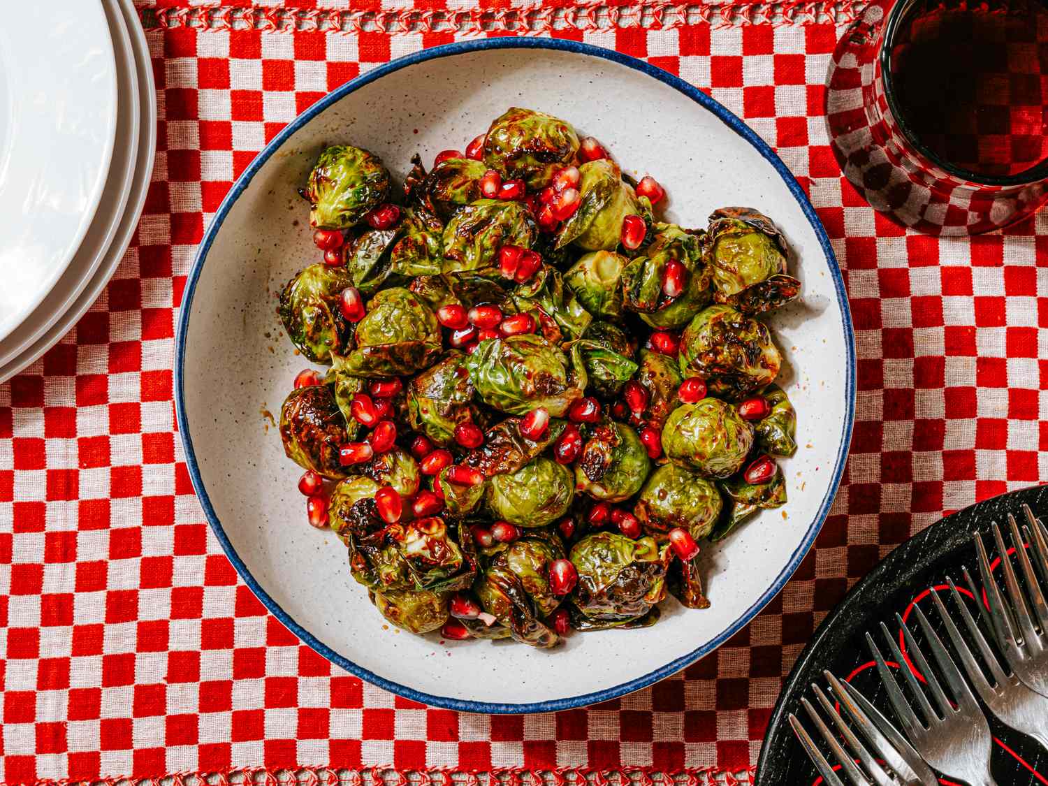 A bowl of roasted Brussels sprouts topped with pomegranate seeds on a patterned tablecloth