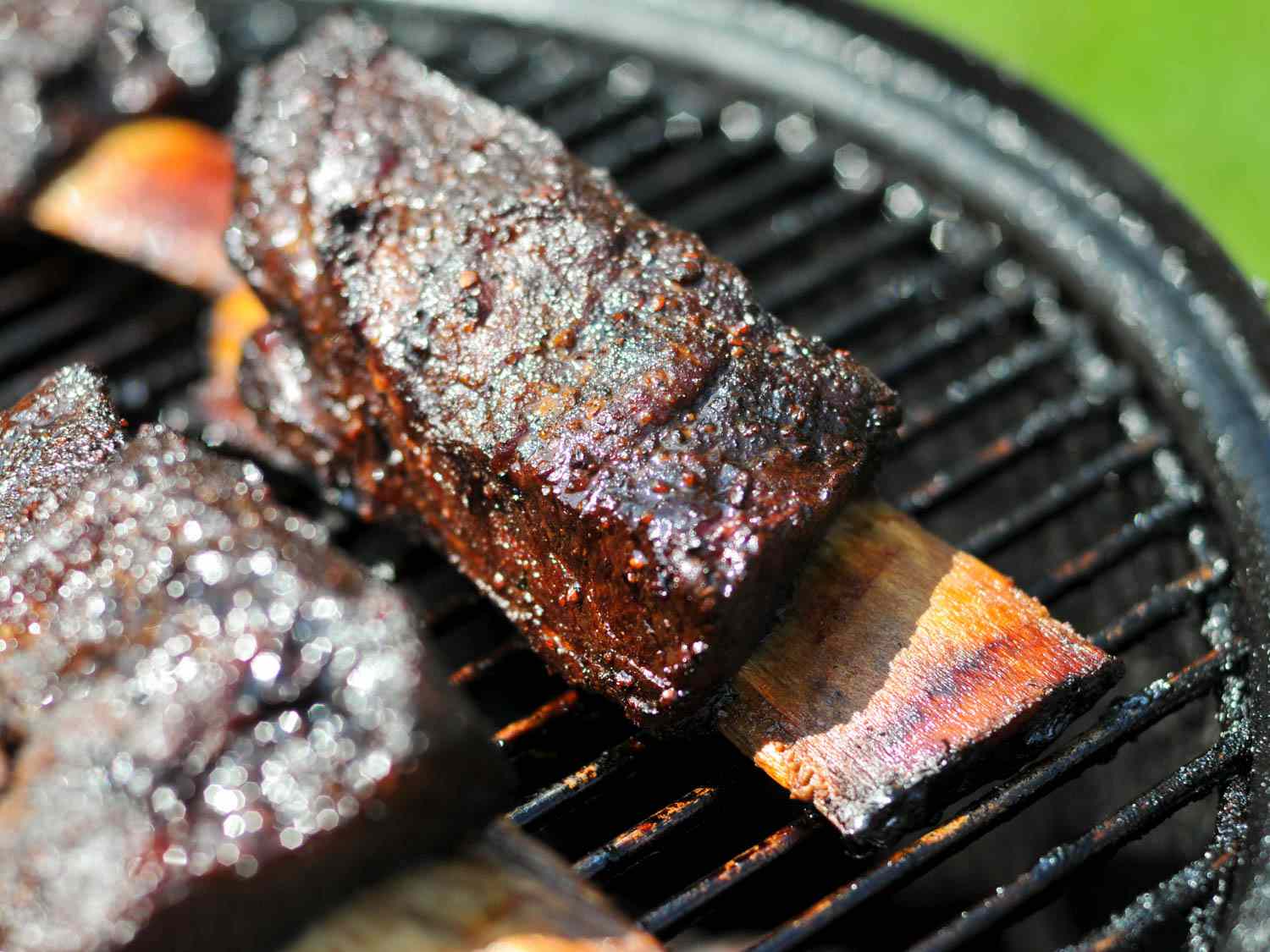 Closeup of barbecue short ribs on the grate of a smoker, ready to eat.