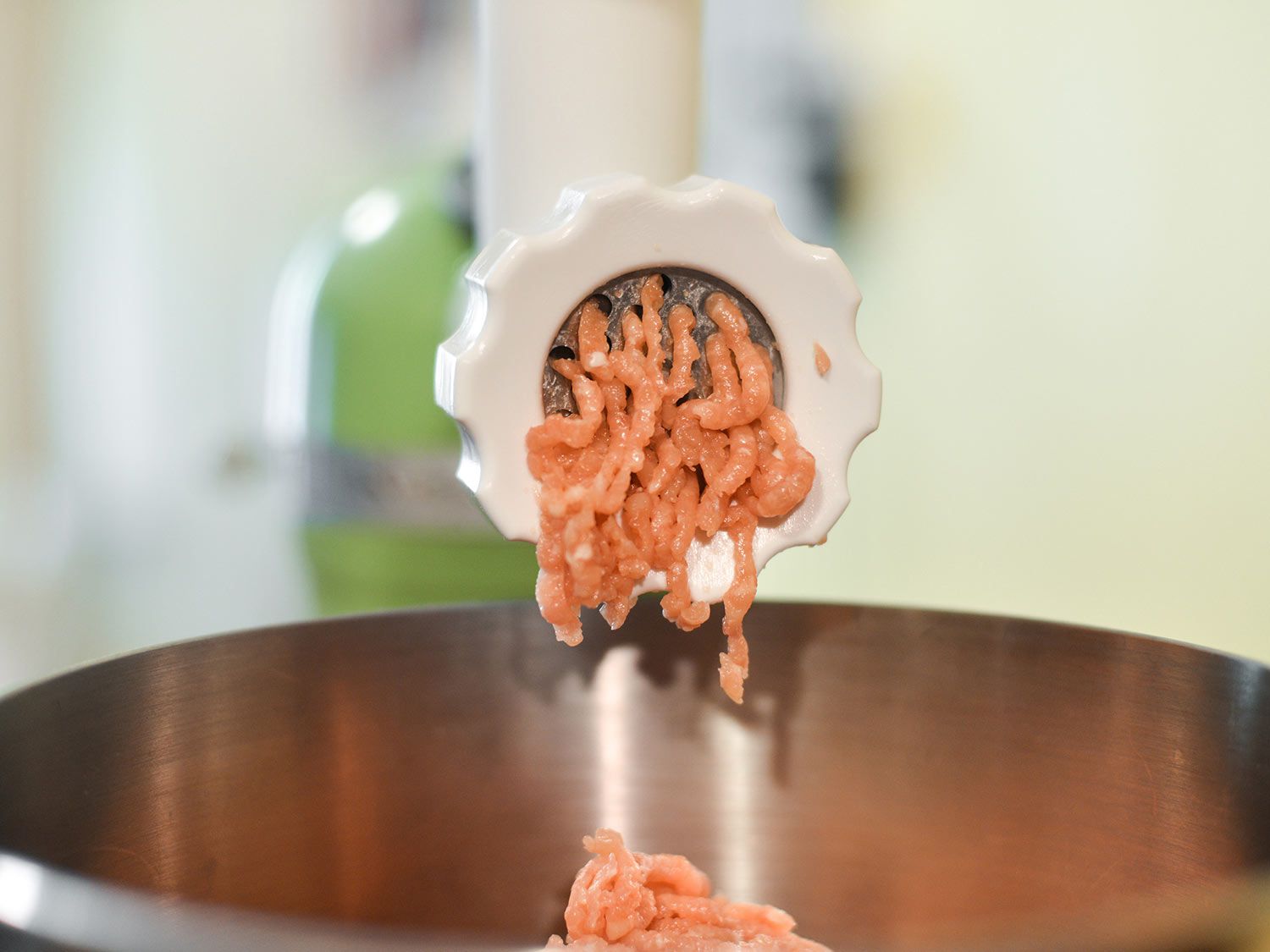 Glistening ground chicken thigh emerging from the meat grinding attachment of a stand mixer.