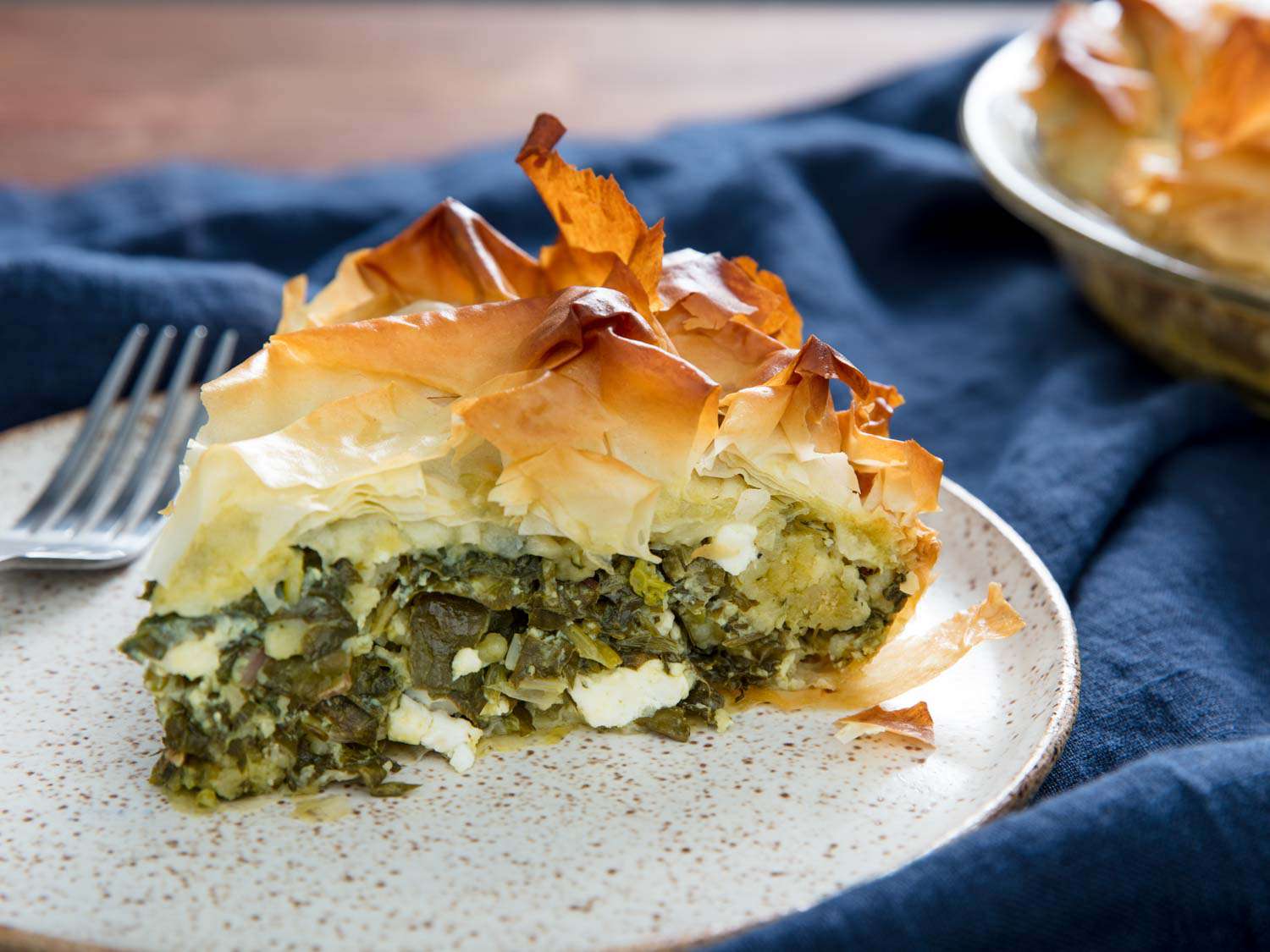 A wedge of spanakopita on a speckled white plate with a fork. 