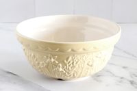 A Mason Cash bowl with embossed floral patterns and a scalloped rim placed on a light surface