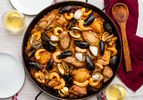 A pan of grilled paella mixta on a table, with mussels, shrimp, chicken, and clams. 