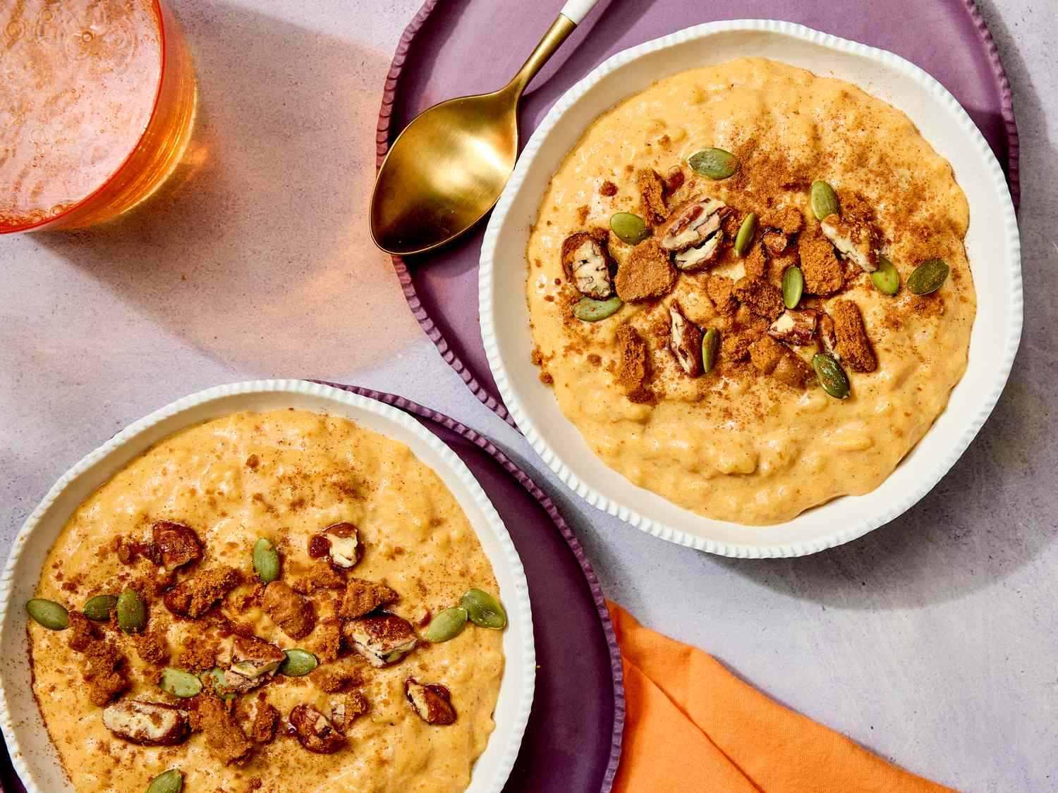 Two bowls of pumpkin rice pudding topped with nuts and seeds on a table setup